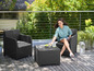 Une femme est assise sur une chaise en osier sur un balcon avec une table basse assortie.
