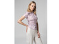 Une femme porte un t-shirt rose à imprimé et un pantalon blanc.
