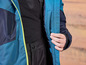 Une veste bleue avec une fermeture éclair jaune et un pantalon noir.