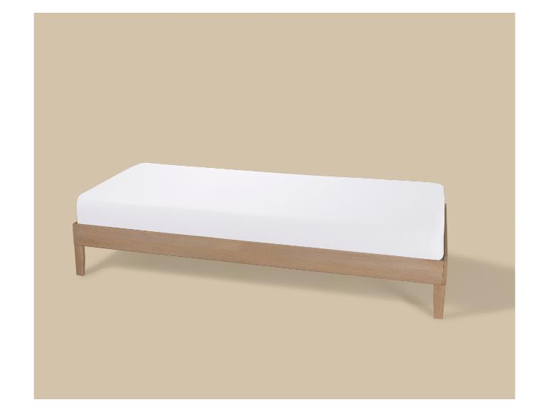 Lit simple en bois avec matelas blanc sur fond beige.