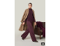 Femme en manteau camel, pull bordeaux et pantalon assorti, marchant à côté d'un canapé en cuir.