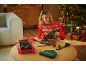 Femme en pull de Noël utilisant un pistolet à colle pour emballer des cadeaux, avec des bonnets sur la table.