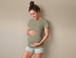 Une femme enceinte portant un t-shirt vert et un short rayé.