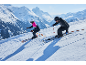 Deux skieurs en tenue de ski et casques dévalent une pente enneigée.