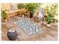Tapis d'extérieur géométrique, mobilier de jardin en rotin et plantes vertes.