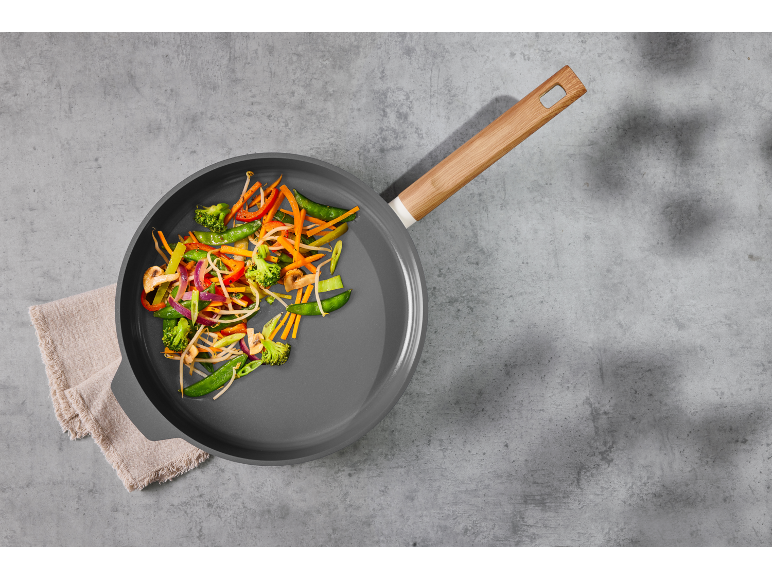 Poêle avec poêlée de légumes sur fond gris.