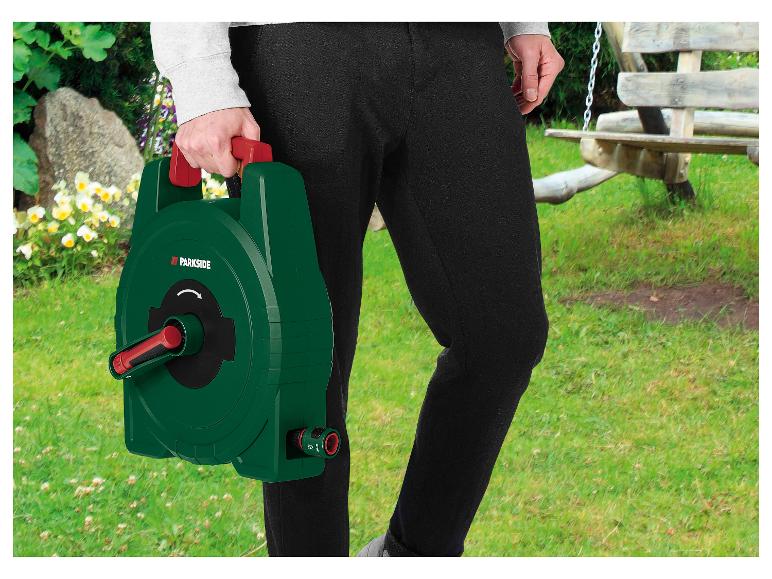 Personne tenant un enrouleur de tuyau vert avec une poignée rouge dans un jardin.