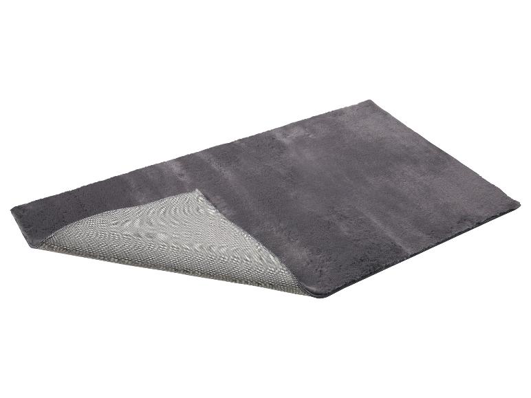 Tapis gris à poils longs avec envers antidérapant, partiellement replié.