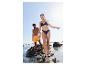 Femme en bikini bleu marine et homme en short orange sur une plage rocheuse.