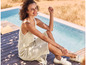 Une femme en robe blanche en tricot et en espadrilles se détend au bord d'une piscine.