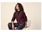 Femme en cardigan tricoté bordeaux, col roulé noir et pantalon en cuir noir assise sur une chaise.