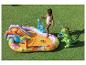 Piscine gonflable thème dinosaures avec toboggan et arroseur, avec une petite fille qui joue.