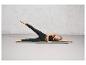 Femme en leggings noirs et soutien-gorge de sport sur un tapis de yoga gris.