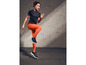 Une femme en t-shirt noir et leggings orange fait de l'exercice.