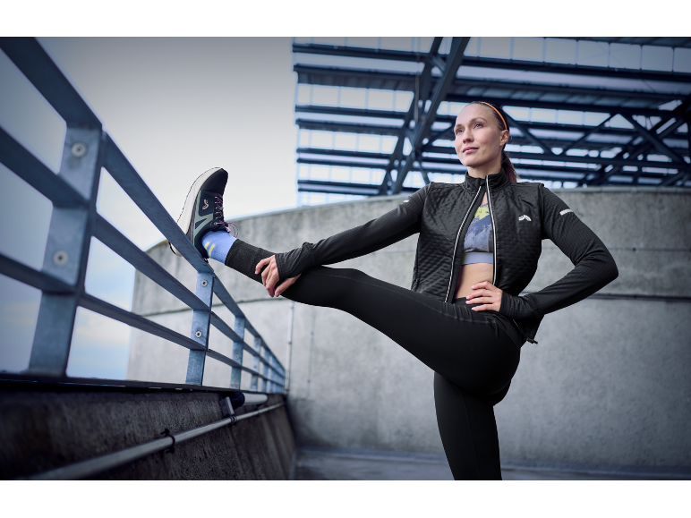 Femme en tenue de sport et chaussures de course s'étirant sur une balustrade.