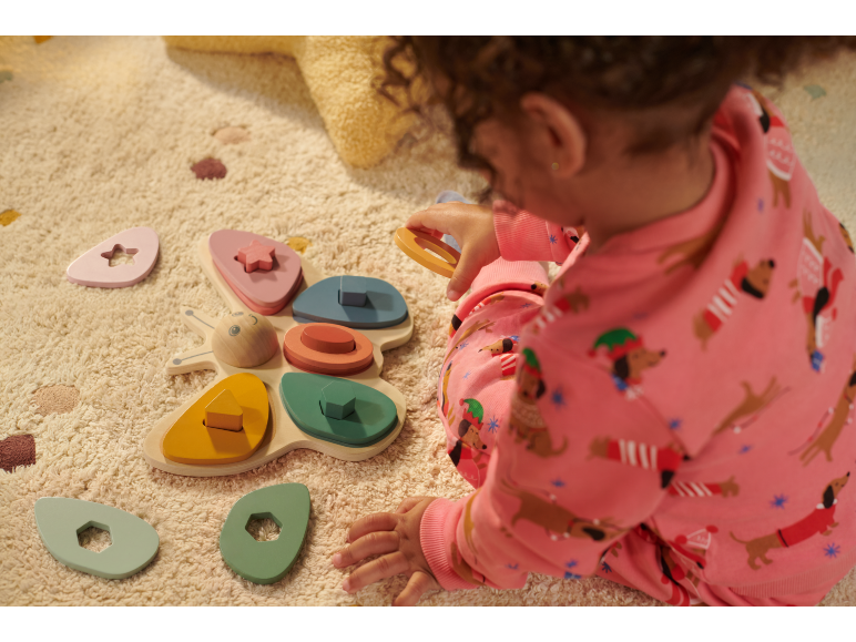 Bébé joue avec un jouet de tri en bois en forme de papillon sur un tapis clair.