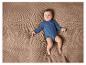 Bébé dans un body bleu allongé sur une couverture tricotée.