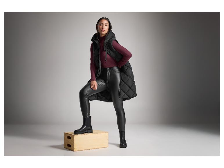 Femme en veste matelassée noire, pull bordeaux et bottes noires.