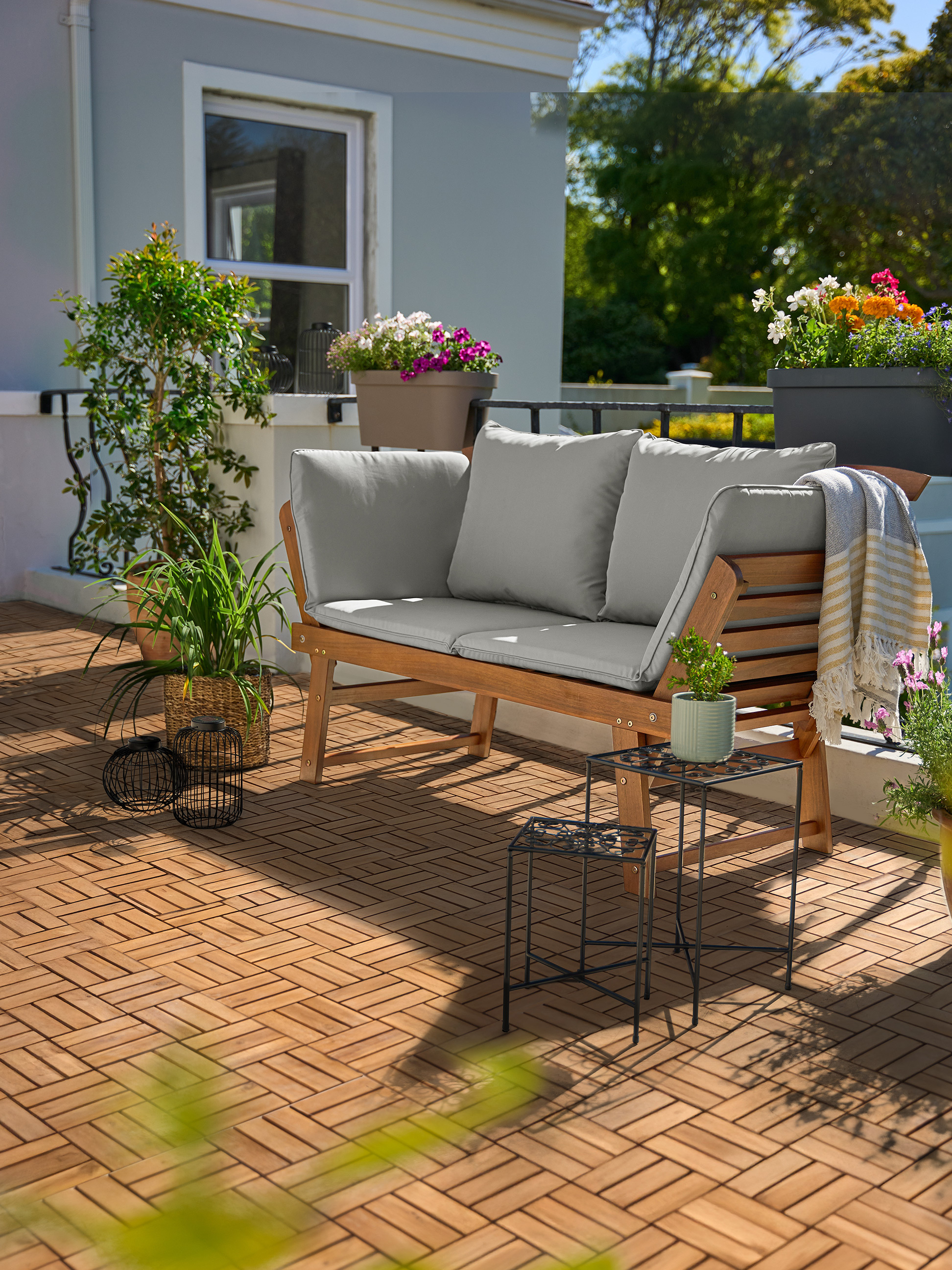 Canapé de jardin en bois avec coussins gris sur un balcon avec dalles de bois et plantes