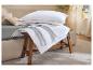 Oreillers et couettes blancs avec passepoil bleu sur un tabouret en bois près d'un lit.