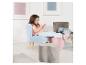 Une jeune fille assise sur une chaise en velours bleu, les pieds posés sur des poufs roses et gris.