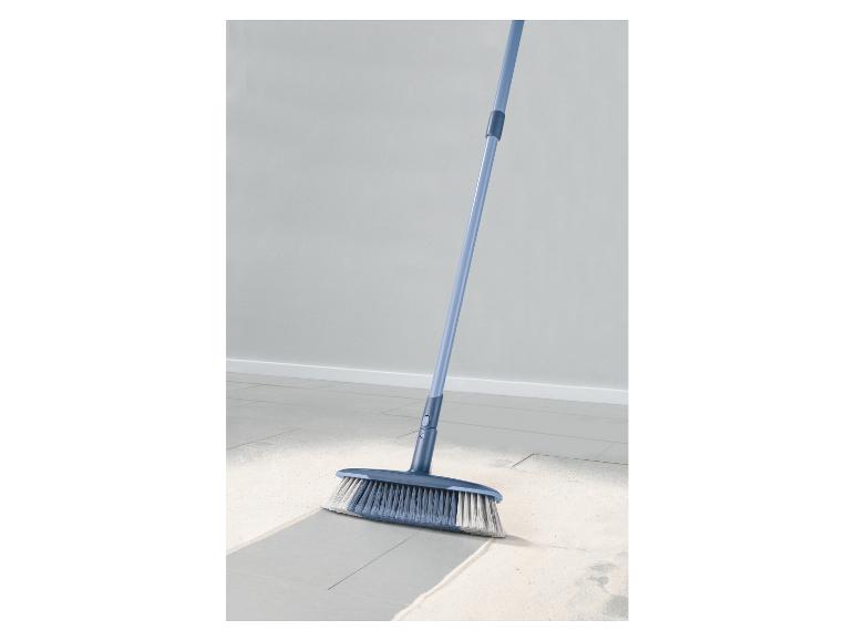 Balai bleu balayant un sol poussiéreux.