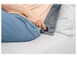 Une femme assise sur un canapé gris avec un coussin chauffant