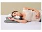 Femme dormant sur le côté sur un lit avec un oreiller ergonomique gris et blanc.