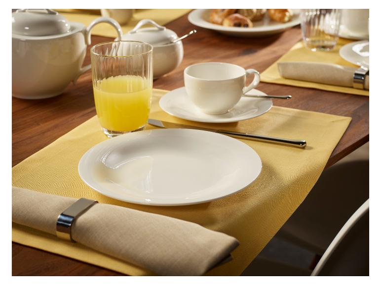 Table de petit-déjeuner avec assiettes blanches, tasses, pot, verre de jus et serviettes.
