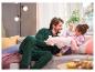 Un père et sa fille jouent avec une licorne en peluche sur le canapé, vêtus de pyjamas verts et roses.