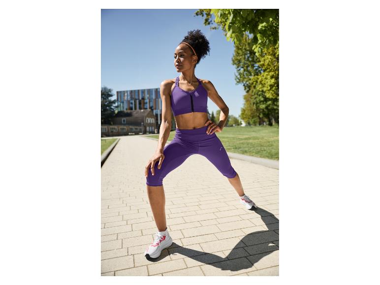Femme en brassière de sport violette et legging capri s'étirant à l'extérieur.