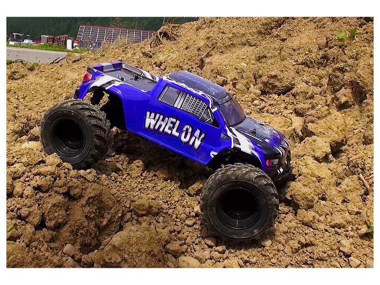 Un monster truck Whelon bleu gravit une colline de terre.