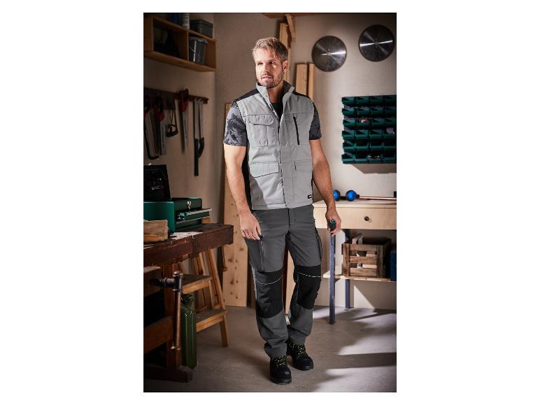 Un homme dans un gilet de travail gris et un pantalon de travail noir dans un atelier.