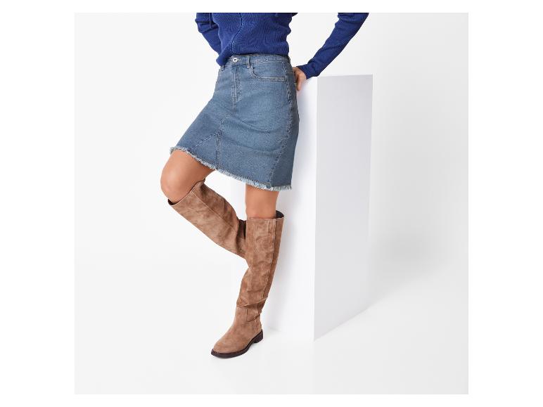 Femme en pull bleu et jupe en jean, bottes hautes brunes.