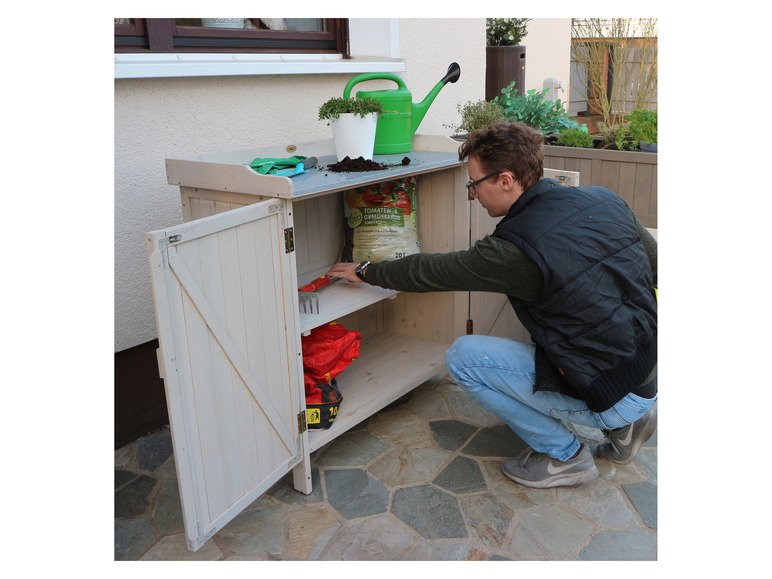 Un homme ouvre un abri de jardin avec des outils de jardinage et de la terre.