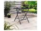 Table de jardin pliante gris foncé sur une terrasse avec des plantes et un jardin en arrière-plan.