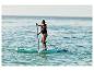 Femme pagayant sur une planche de paddleboard en mer, portant un gilet de sauvetage.