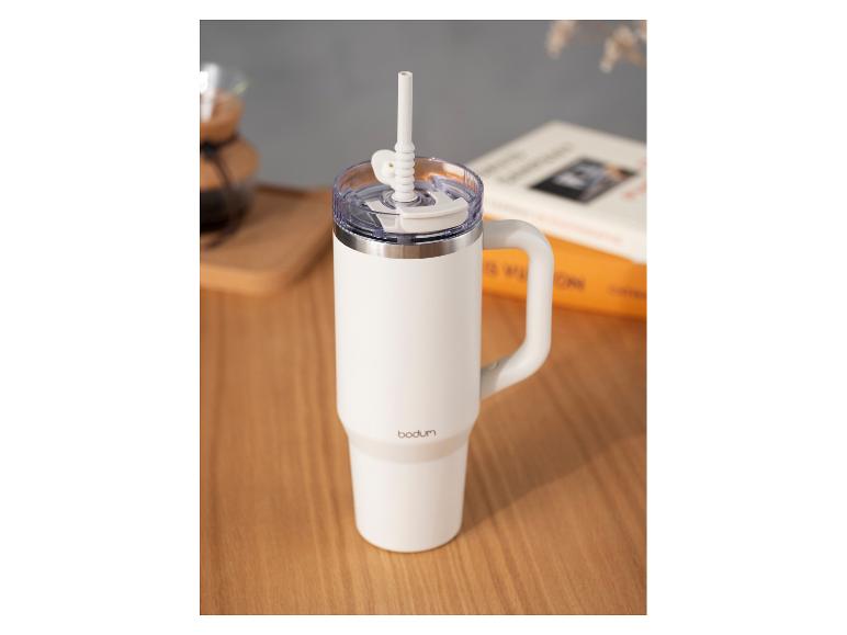 Mug de voyage blanc Bodum avec anse et paille sur une table en bois.