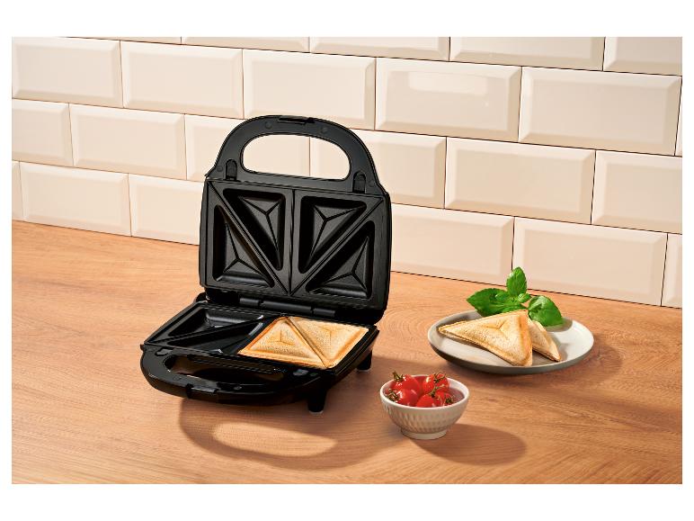 Appareil à croque-monsieur avec croque-monsieur prêts, tomates et basilic sur une surface en bois.