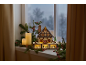 Maison de Noël en bois illuminée sur un rebord de fenêtre avec bougies et branches de sapin