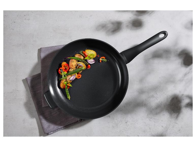Poêle noire avec des pommes de terre rôties, des légumes et des herbes sur un torchon gris.