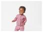 Un jeune enfant sourit en portant un cardigan et un pantalon roses en tricot.