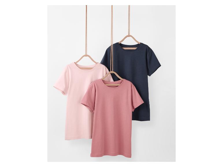 Trois t-shirts unis : rose poudré, rose et marine, suspendus à des cintres.