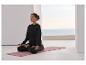 Femme méditant sur un tapis de yoga rose, vêtue d'un sweat-shirt et d'un pantalon noirs.