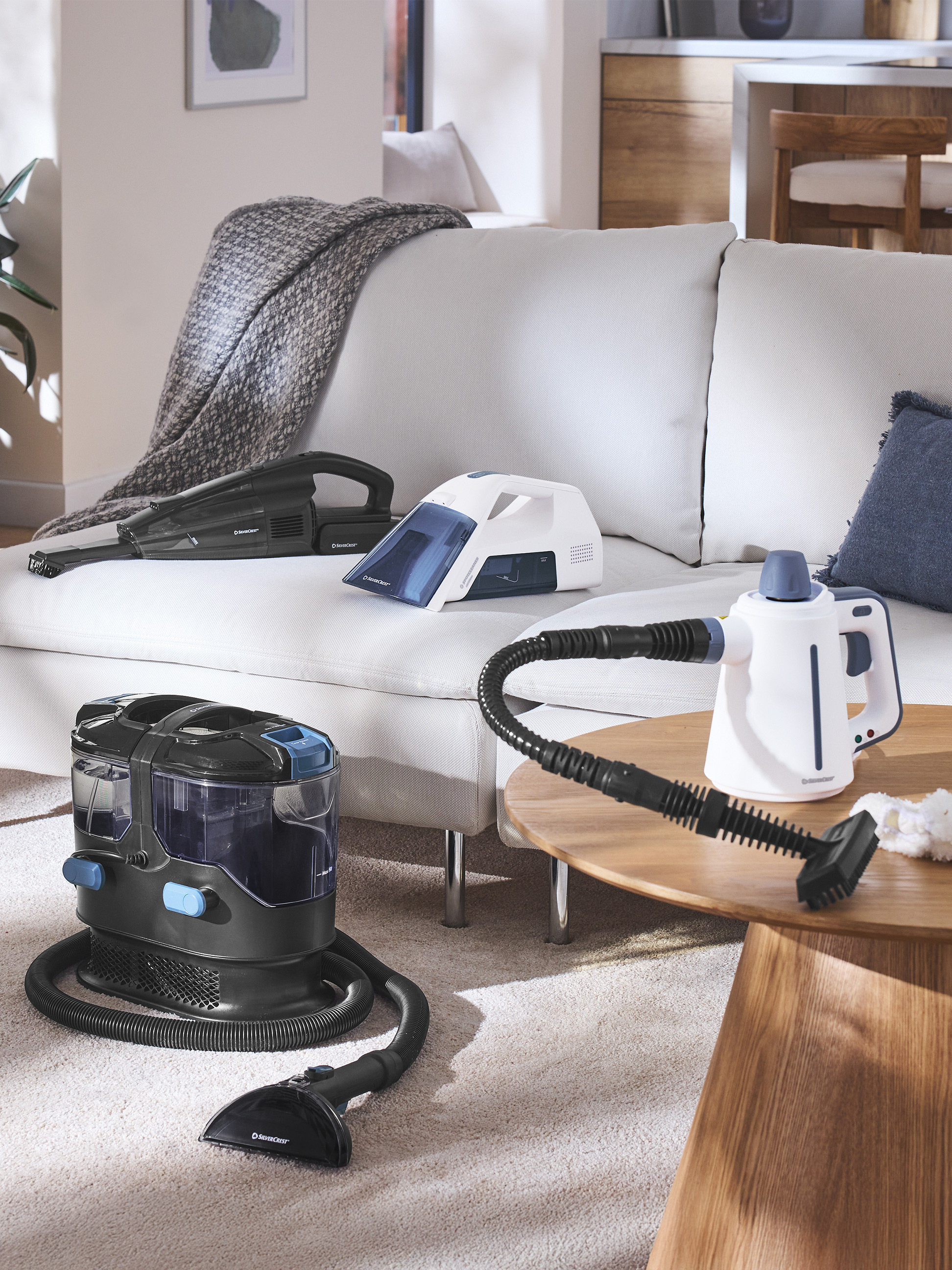 Aspirateurs et nettoyeurs vapeur dans un salon moderne avec canapé et table basse.