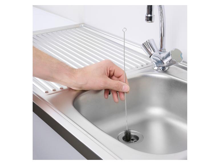 Main nettoyant un évier de cuisine avec une brosse à bouteille.