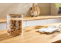 Bocal en verre avec couvercle en bois rempli de granola sur un plan de travail en bois.