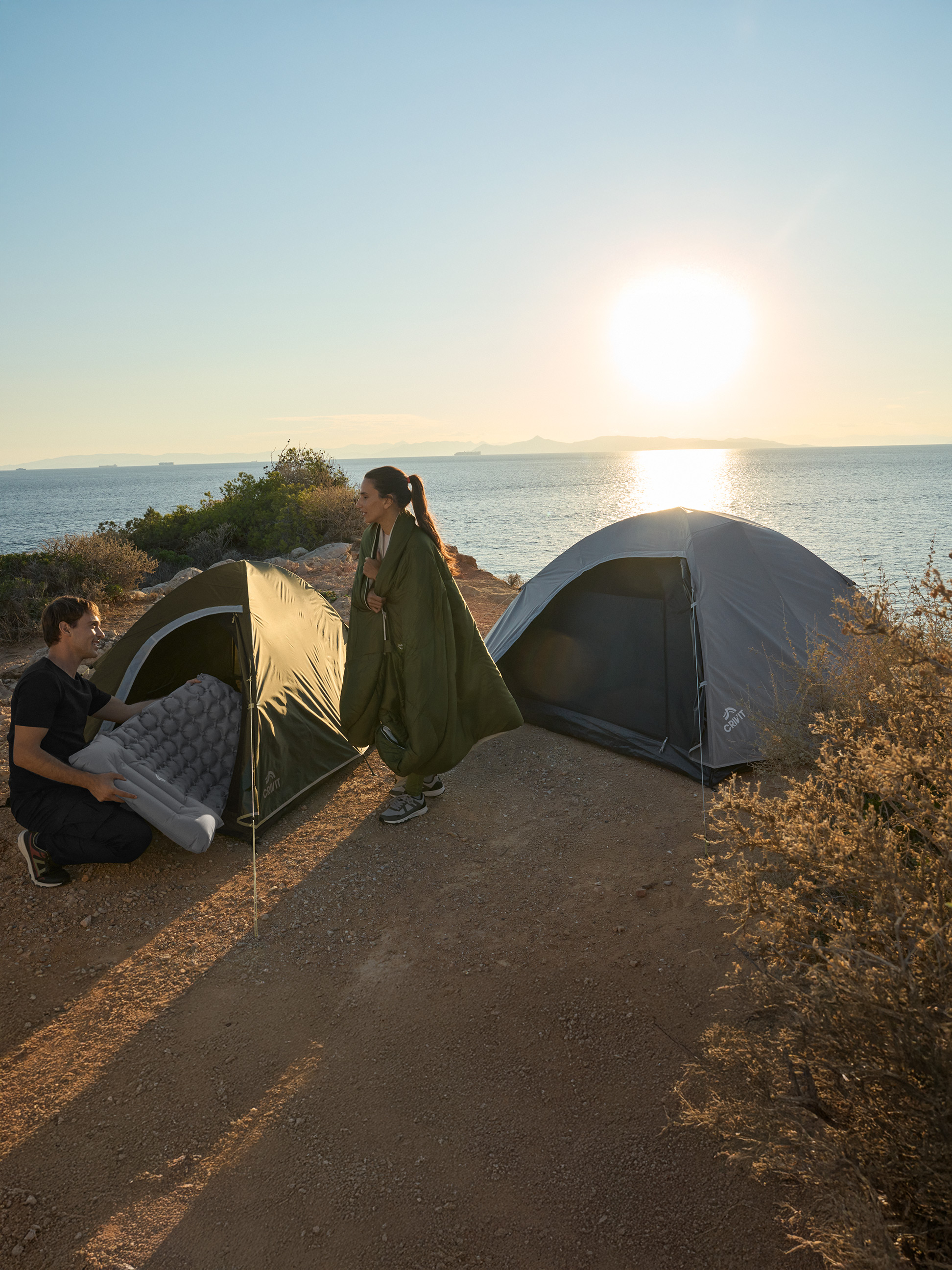 Deux personnes campent au bord de la mer avec deux tentes Crivit et un matelas gonflable.