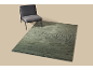 Une chaise grise à côté d'un tapis vert avec un motif tourbillonnant sur un fond beige.