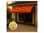 Store banne rayé orange sur une terrasse de maison avec un sceau 'Premium Qualität Made in Germany'.
